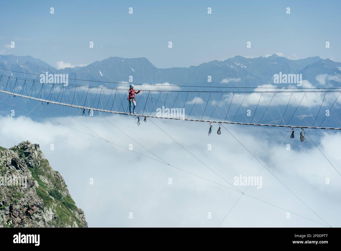 Una persona cammina su un ponte sospeso in corda tra le nuvole. Attrazione estrema. Wanderlust e avventure. Foto Stock