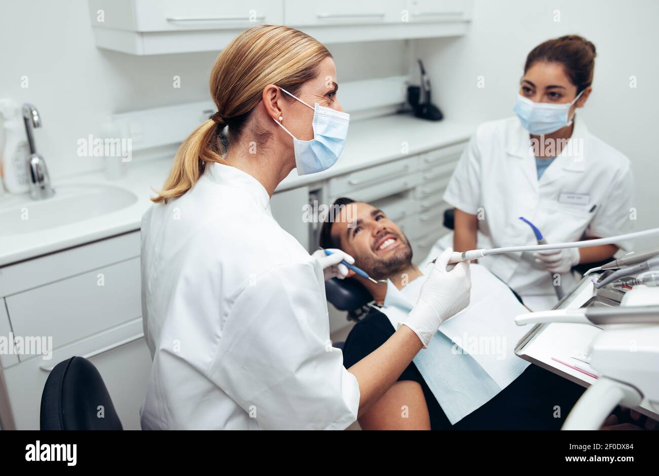 Medico dentale che guarda un monitor mentre si tratta un paziente di sesso maschile. Dentista femminile che indossa la maschera facciale con paziente maschile seduto nel chai dentista Foto Stock