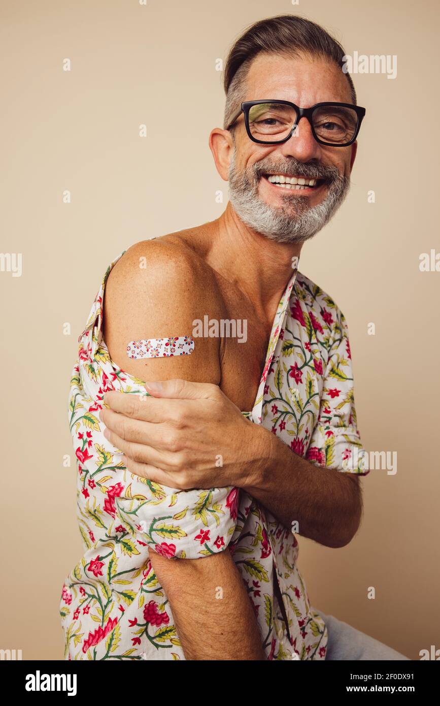 Ritratto di uomo maturo sorridente dopo aver ottenuto il vaccino. Uomo maturo che mostra il braccio con bendaggio dopo aver ricevuto la vaccinazione con virus corona. Foto Stock