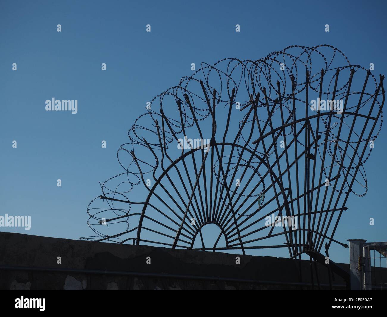 Recinzioni di sicurezza a spirale con filo spinato e sagome contro il cielo blu Foto Stock Recinzioni di sicurezza a spirale con filo spinato e sagome contro il cielo blu Foto Stock