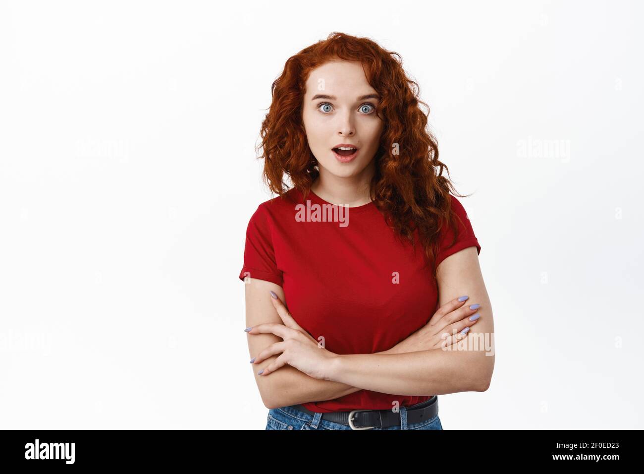 WOW davvero. Sorpresa zenzero ragazza con capelli ricci, bocca aperta e gasping affascinato, fissando impressionato alla macchina fotografica, croce braccia sul petto, bianco Foto Stock