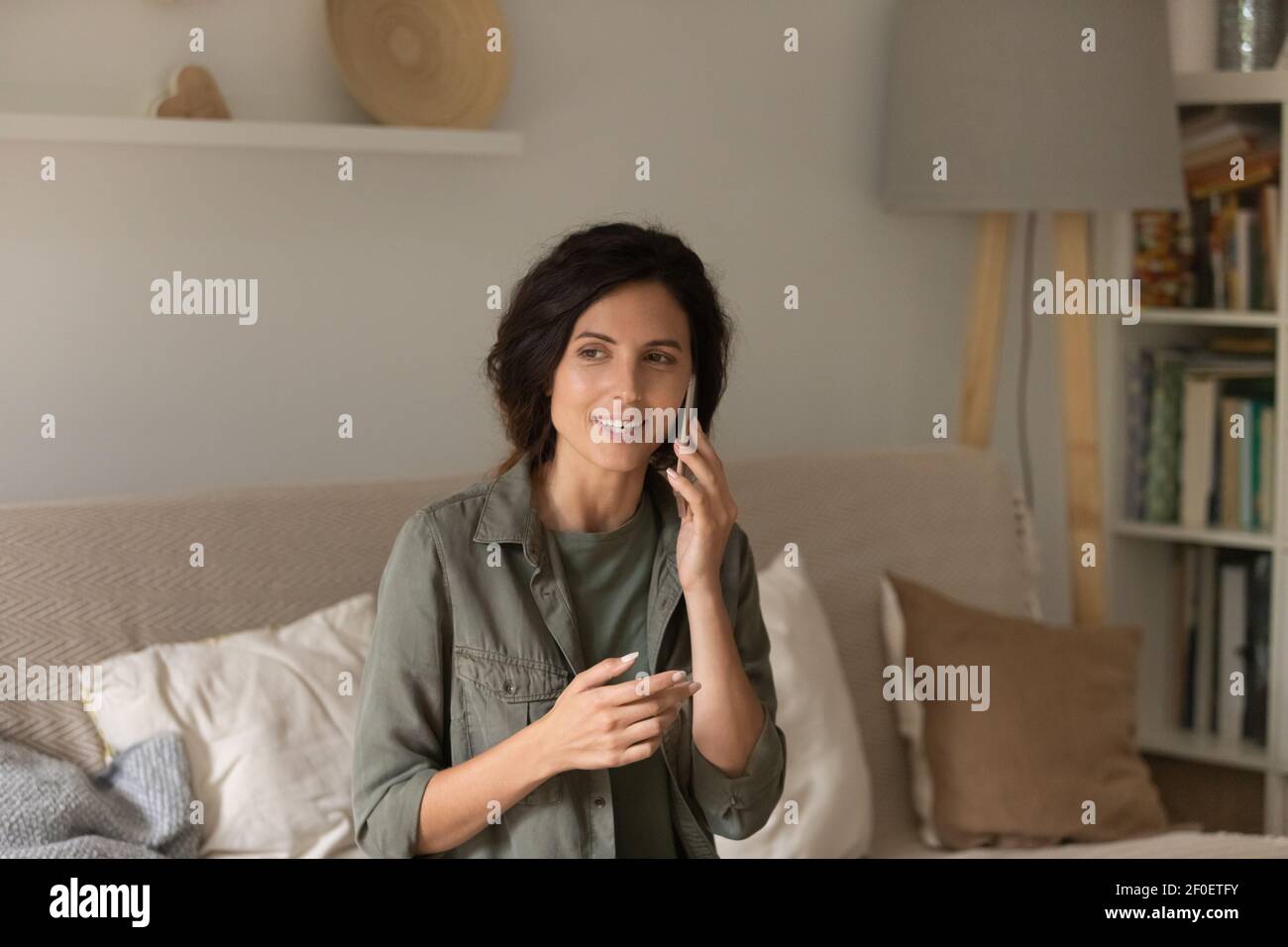 Donna tranquilla millennial godersi la conversazione telefonica tenendo il gadget all'orecchio Foto Stock