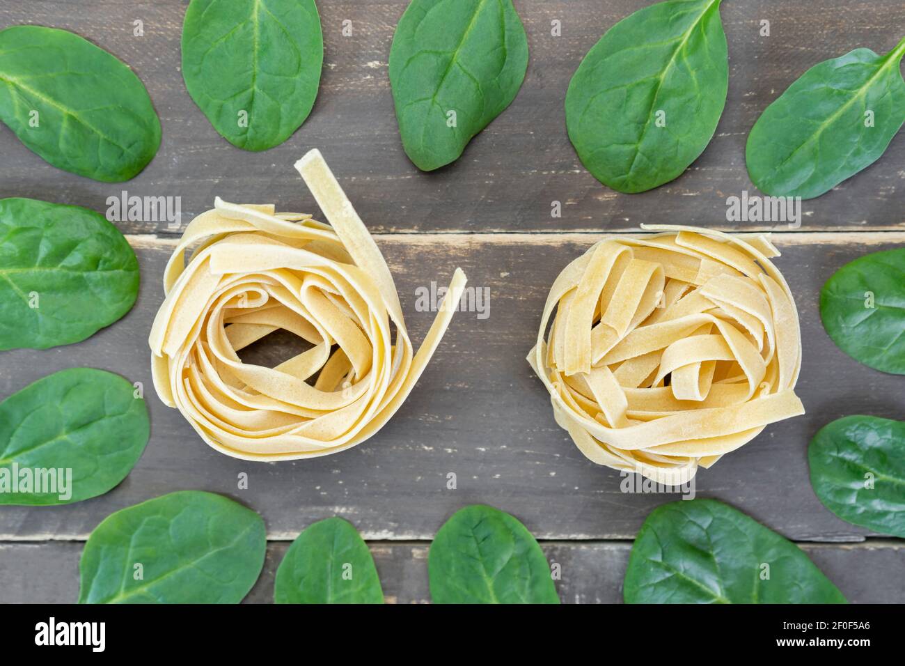 Vista dall'alto tagliatelle crude con foglie di spinaci su tavola di legno.concetto creativo di cibo sano. Foto Stock