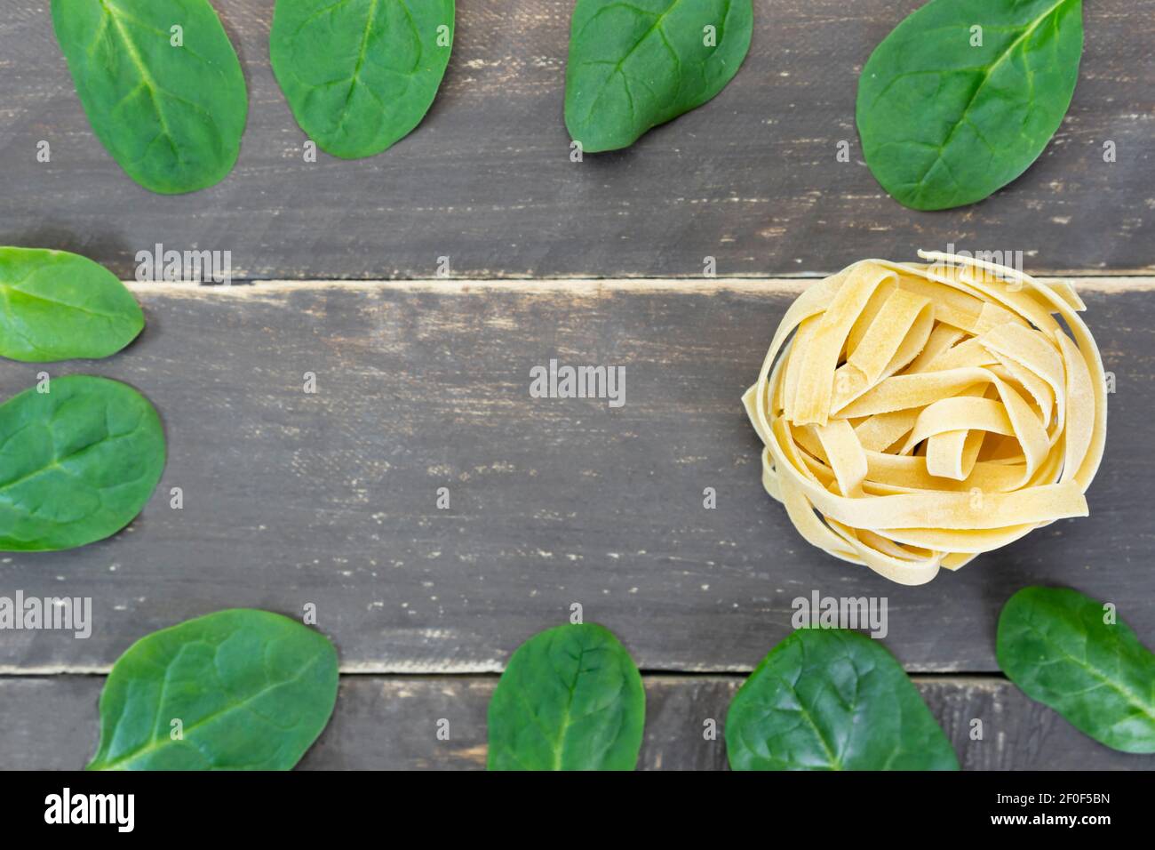 Vista dall'alto tagliatelle crude con foglie di spinaci su tavola di legno.concetto di cibo sano creativo con spazio di copia . Foto Stock