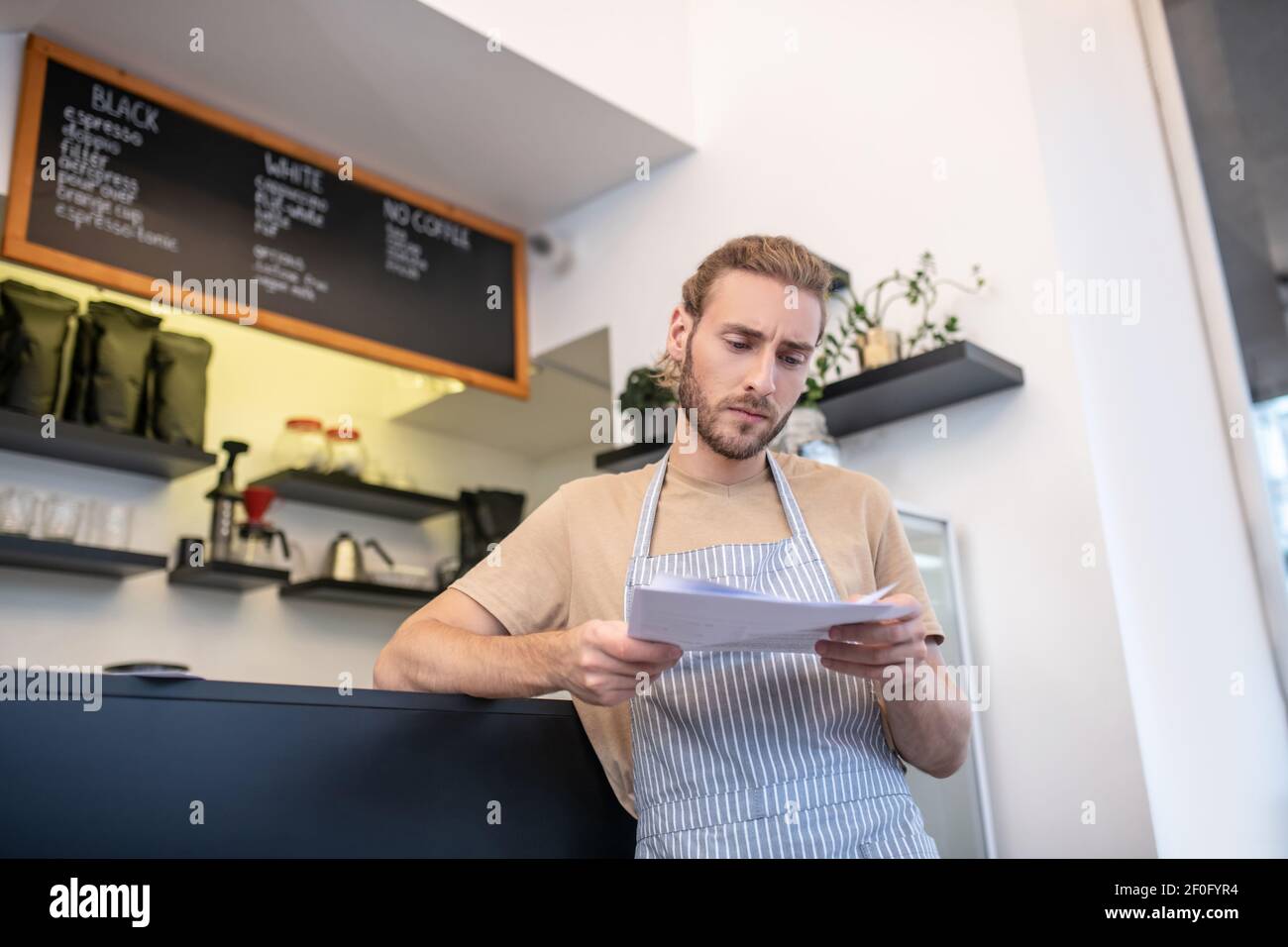 Uomo che legge documenti in piedi nel suo caffè Foto Stock