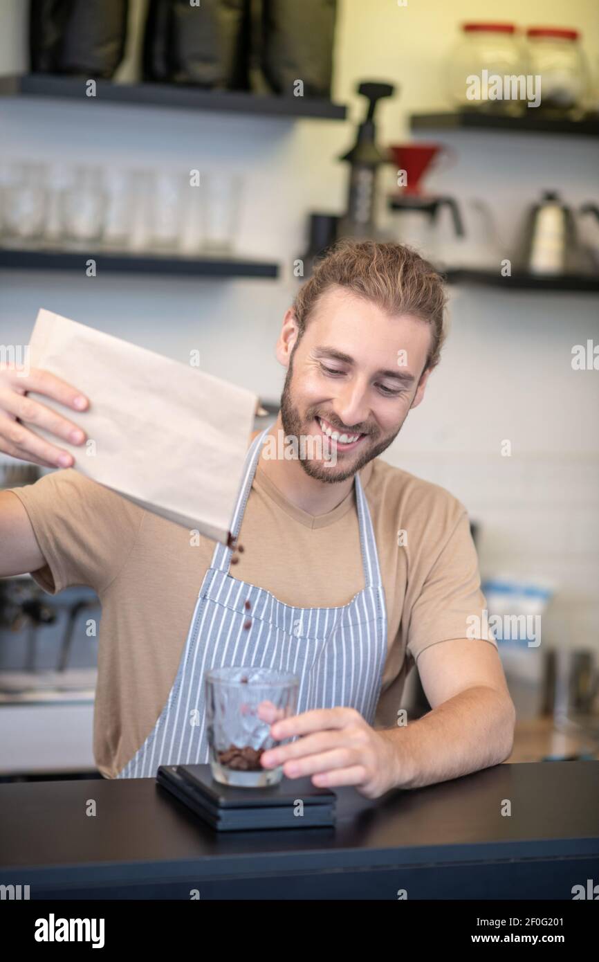 Uomo soddisfatto che versa i chicchi di caffè in un bicchiere Foto Stock