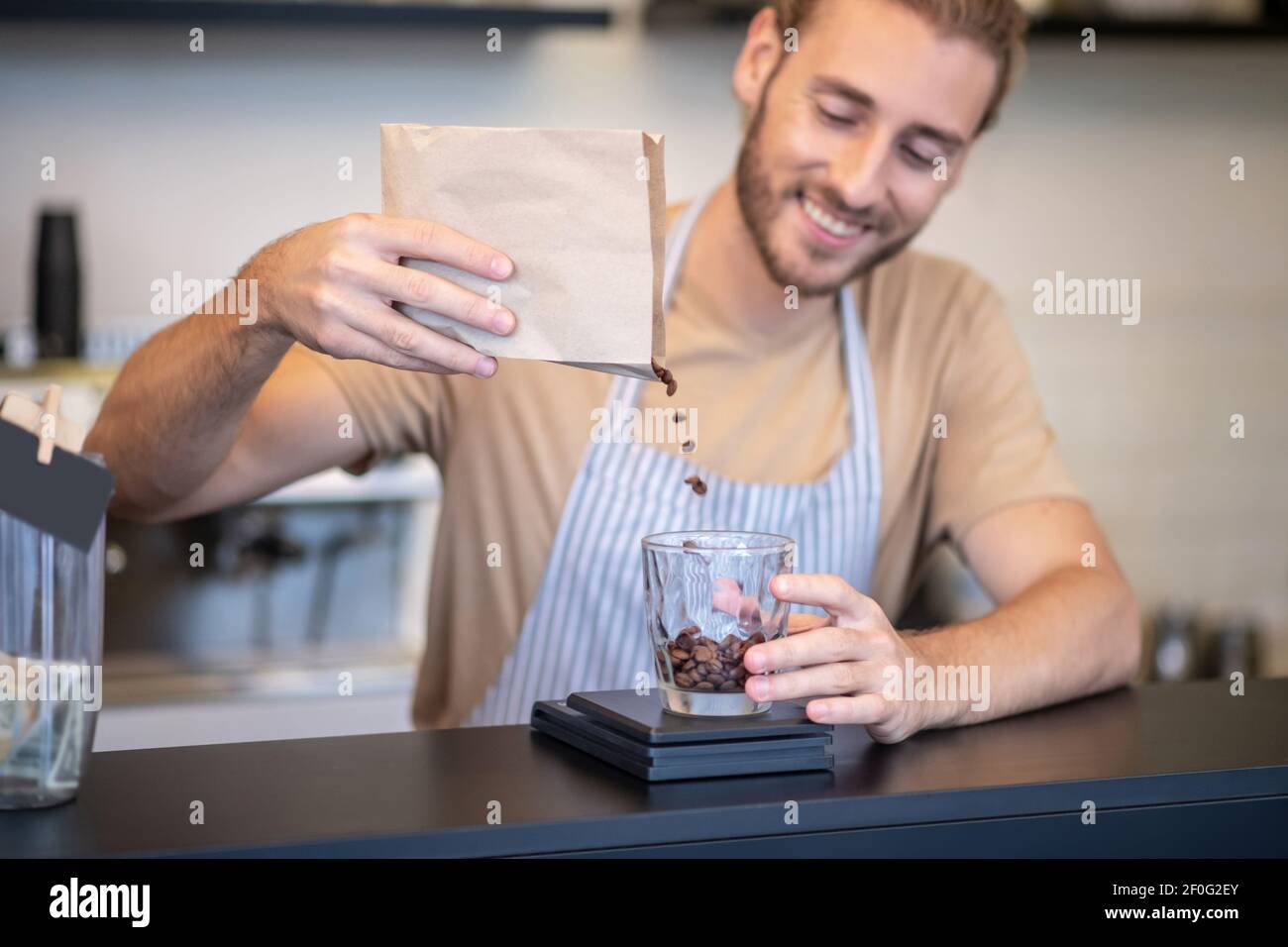 Uomo sorridente al bar che versa i chicchi di caffè Foto Stock