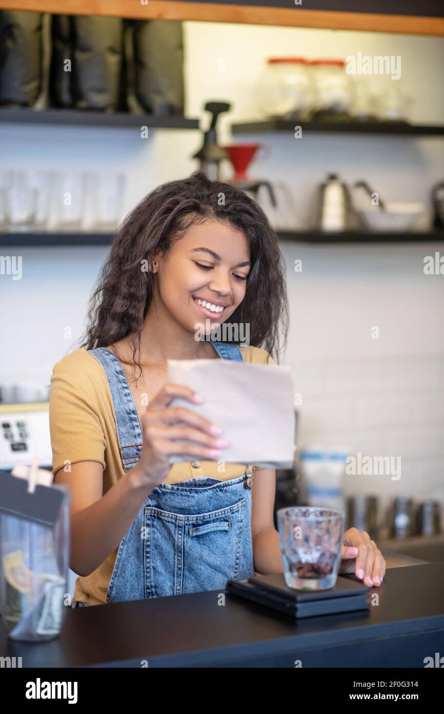 Donna sorridente che versa i chicchi di caffè in vetro Foto Stock