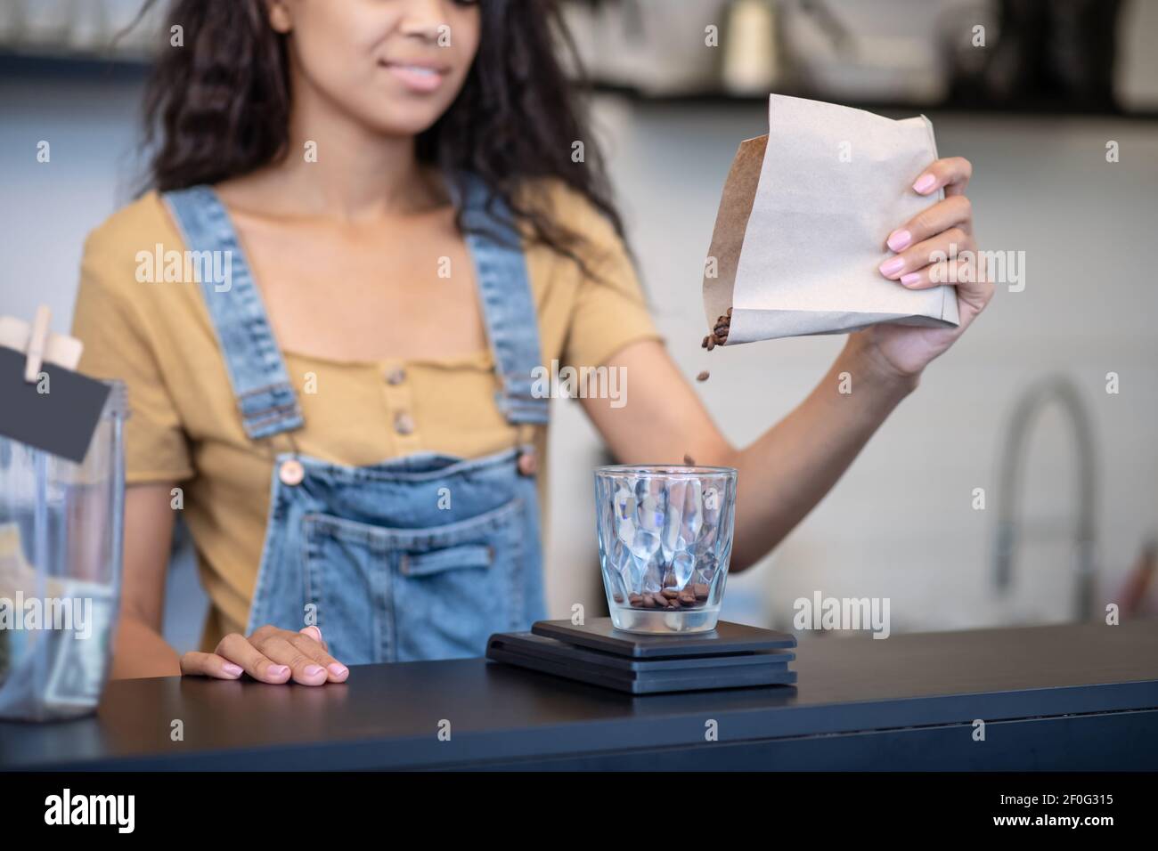 La mano femminile versa i chicchi di caffè nel dosatore Foto Stock