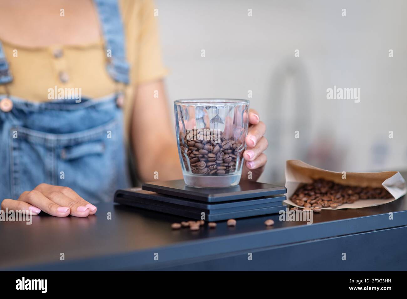 Womans mano mettendo il bicchiere con i chicchi di caffè sulla bilancia Foto Stock
