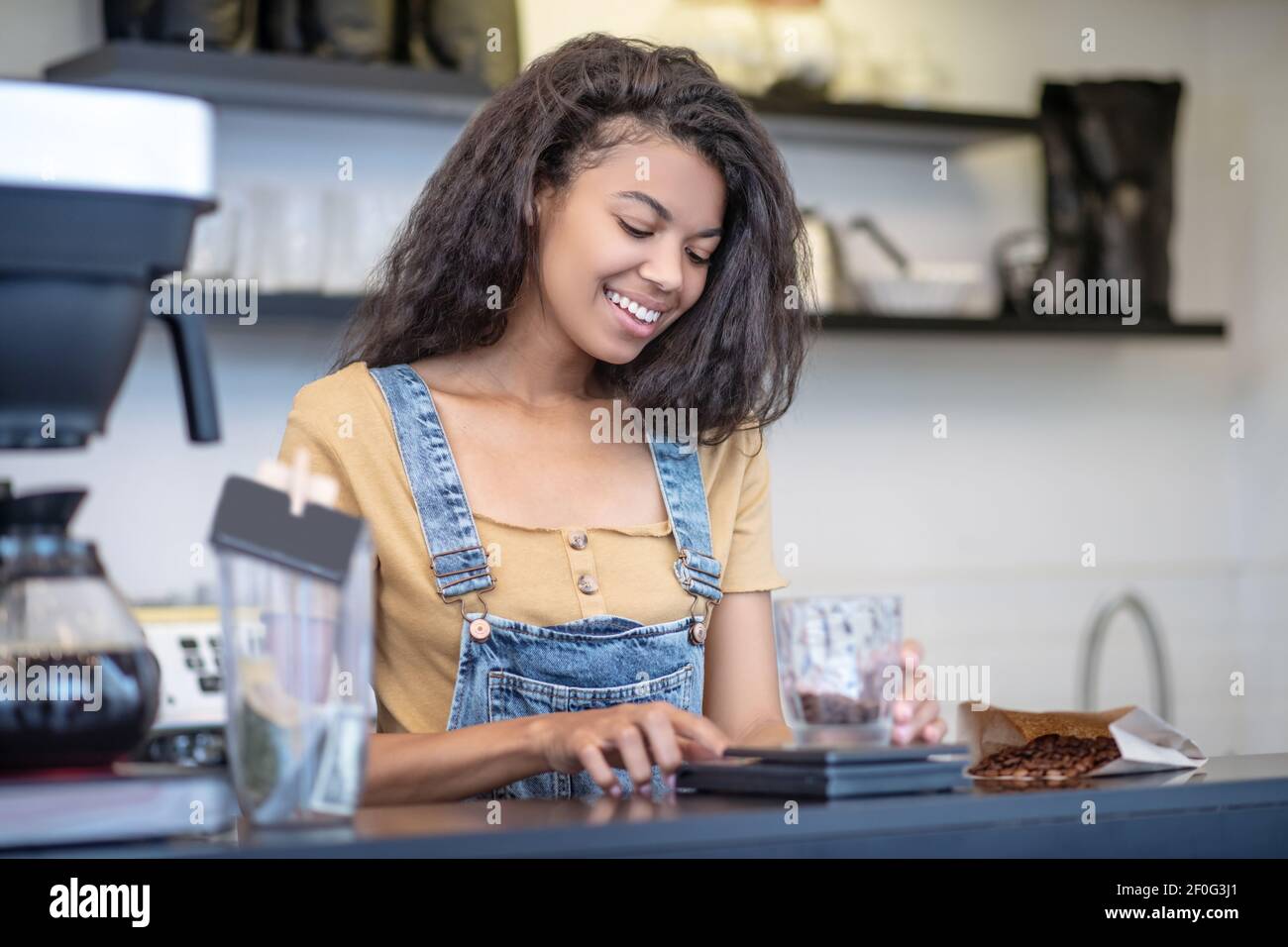 Donna attenta che misura accuratamente i chicchi di caffè dietro il bancone Foto Stock