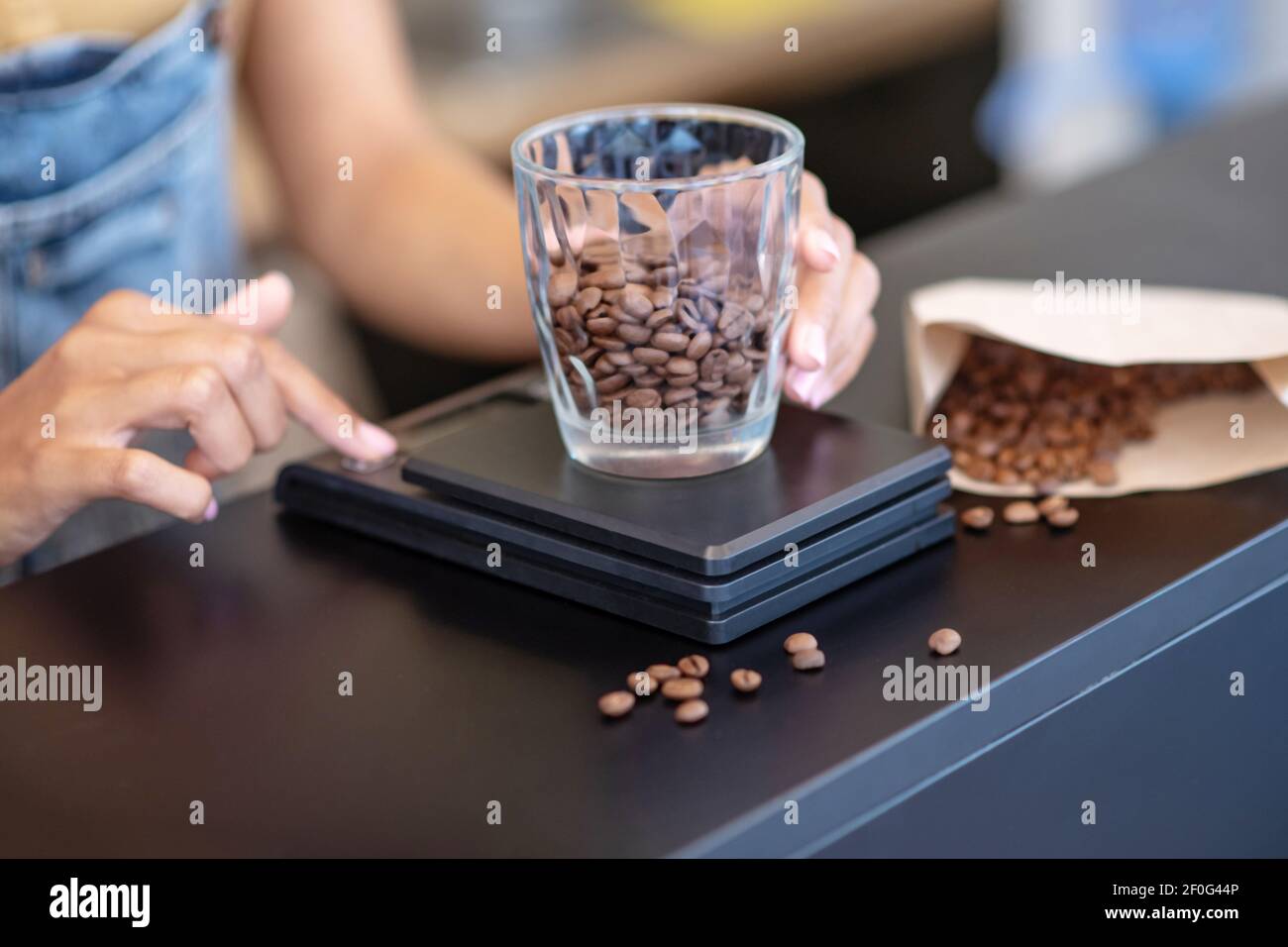 Le mani femminili pesano i chicchi di caffè in vetro Foto Stock