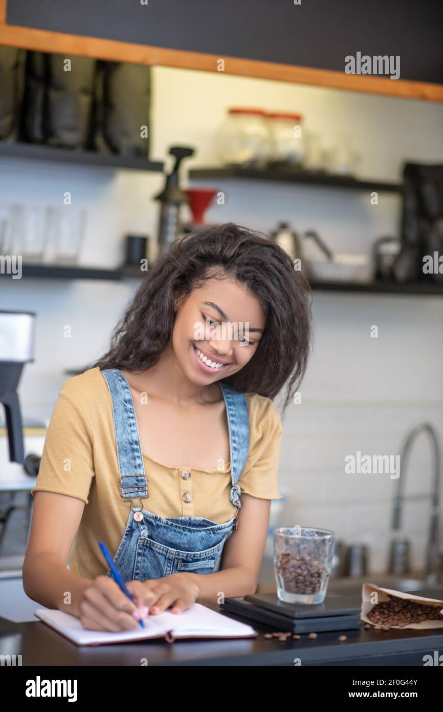 Donna allegra che scrive il peso dei chicchi di caffè nel notebook Foto Stock
