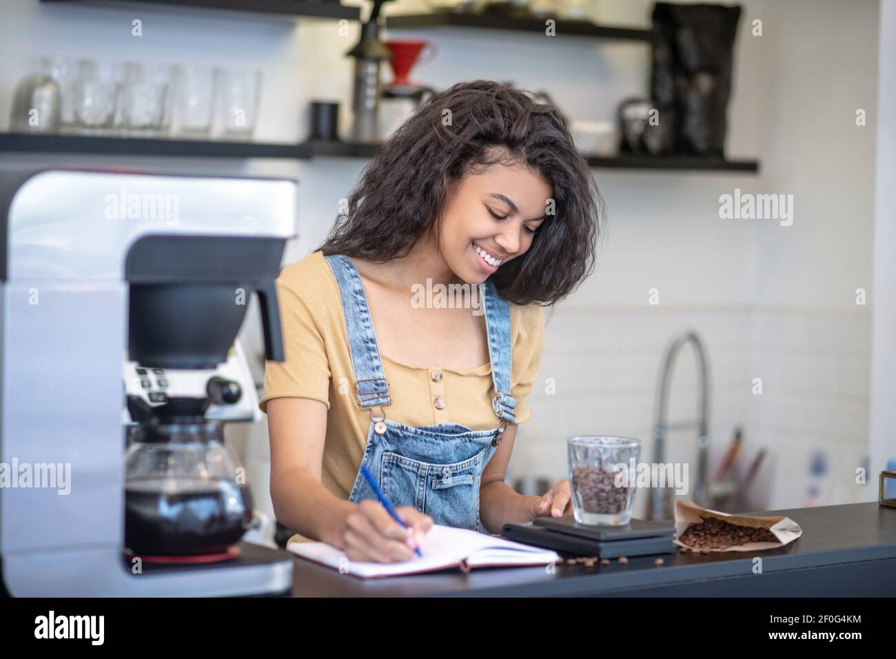 Donna focalizzata che scrive il peso esatto dei chicchi di caffè Foto Stock