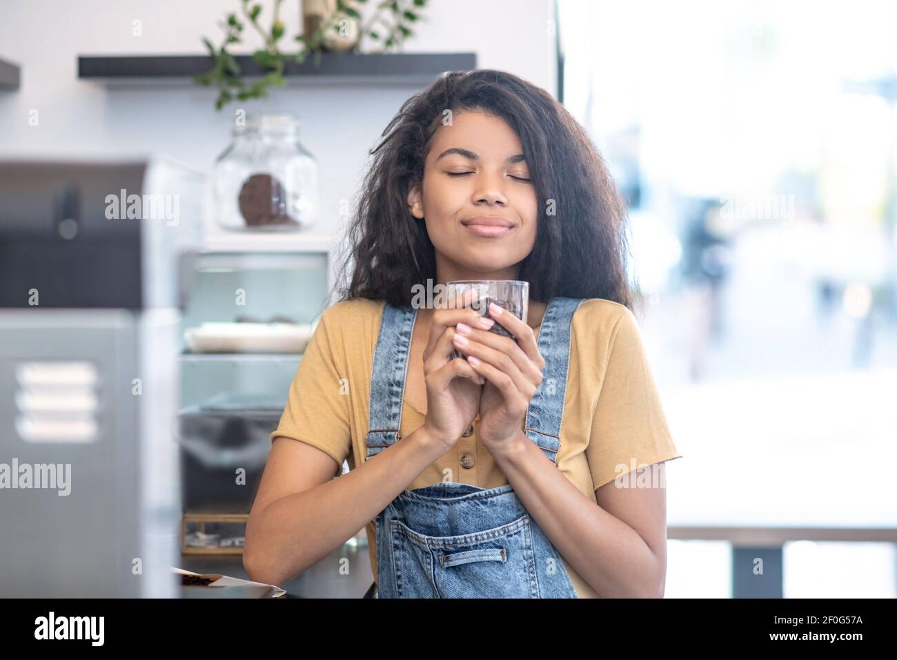 Donna a occhi chiusi con un bicchiere di chicchi di caffè Foto Stock