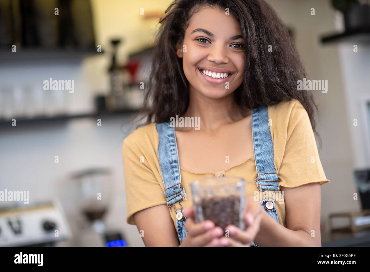 Donna sorridente che tiene fuori un bicchiere di chicchi di caffè Foto Stock