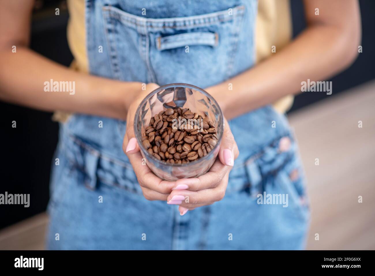 Mani femminili che tengono un bicchiere di chicchi di caffè Foto Stock