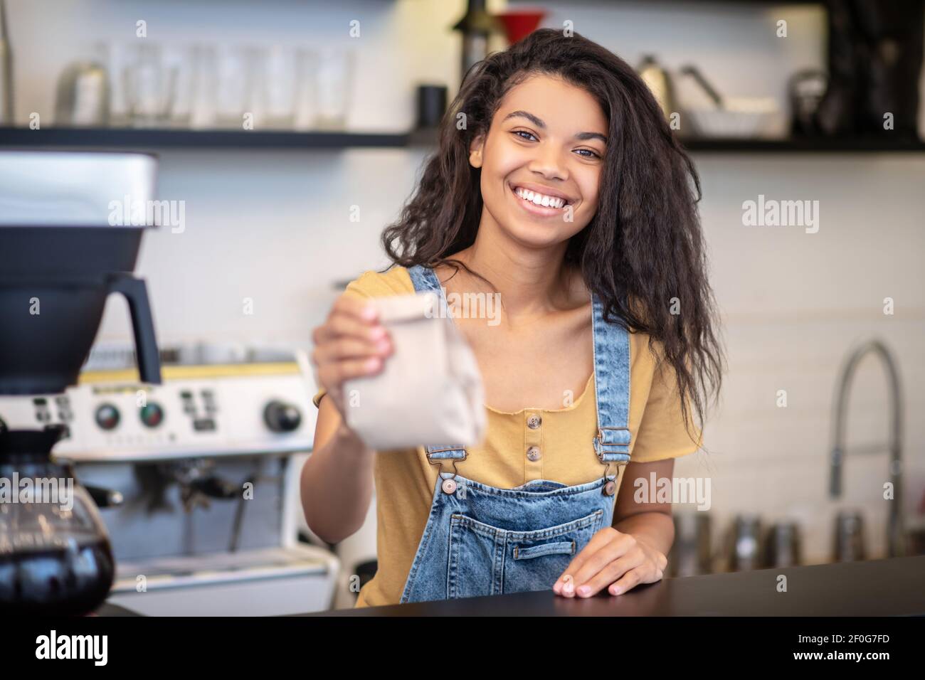 Donna allegra al banco che tiene fuori il sacchetto di carta Foto Stock