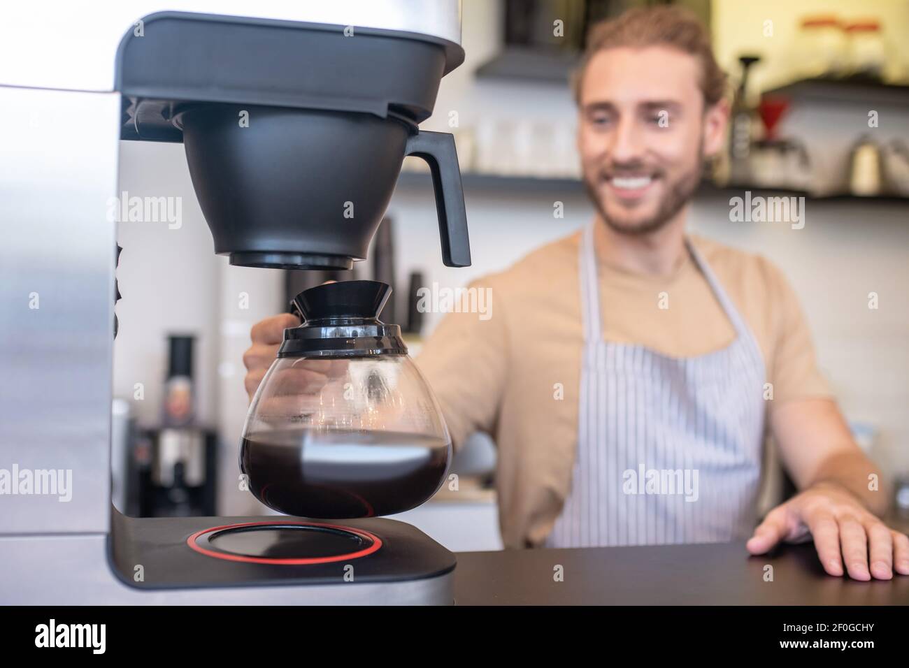 Uomo che prende la caraffa di vetro del caffè dalla macchina per il caffè Foto Stock