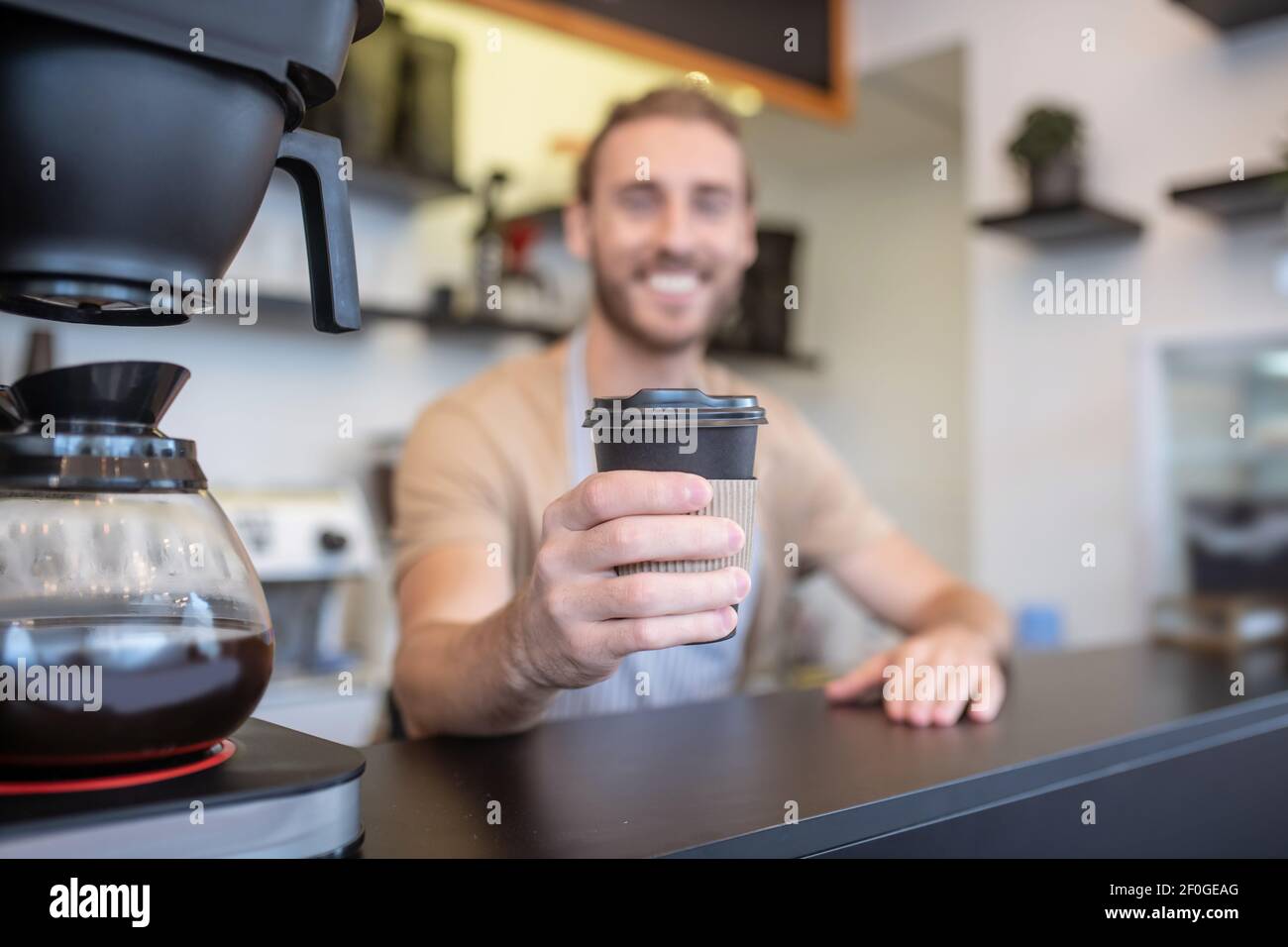 Bicchiere di caffè in mano estensibile del barista sorridente Foto Stock