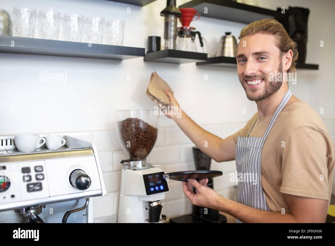 Uomo sorridente vicino al macinacaffè nel suo caffè Foto Stock