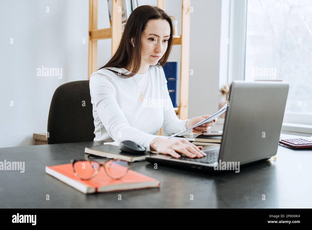 Processi finanziari di contabilità remota. Soluzione di contabilità online. Ritratto sincero di una ragioniere femminile che lavora con computer portatile, calcolatrice e documenti a casa Foto Stock