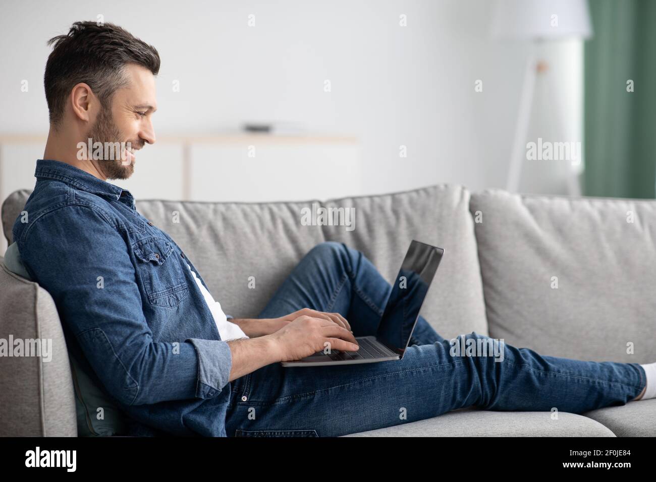 Vista laterale di un uomo reclinato sul divano, utilizzando un computer portatile Foto Stock