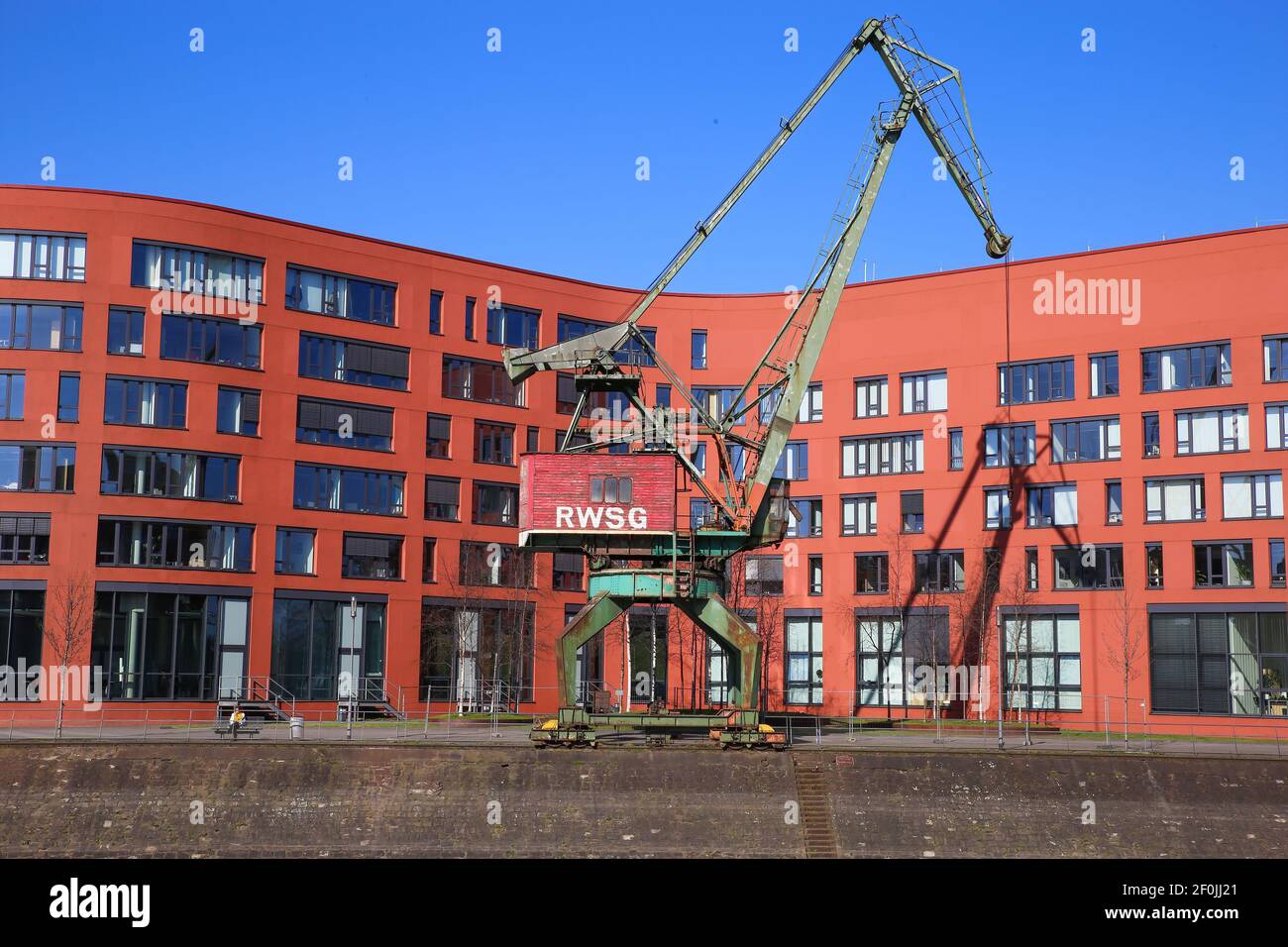 Duisburg (innenhafen), Germania - 1 marzo. 2021: Vista su una vecchia gru in acciaio con edifici industriali di uffici rossi nel porto interno del reno contro il cielo blu Foto Stock