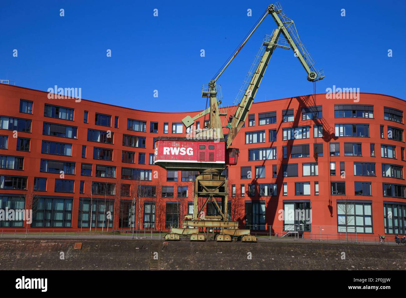 Duisburg (innenhafen), Germania - 1 marzo. 2021: Vista su una vecchia gru in acciaio con edifici industriali di uffici rossi nel porto interno del reno contro il cielo blu Foto Stock