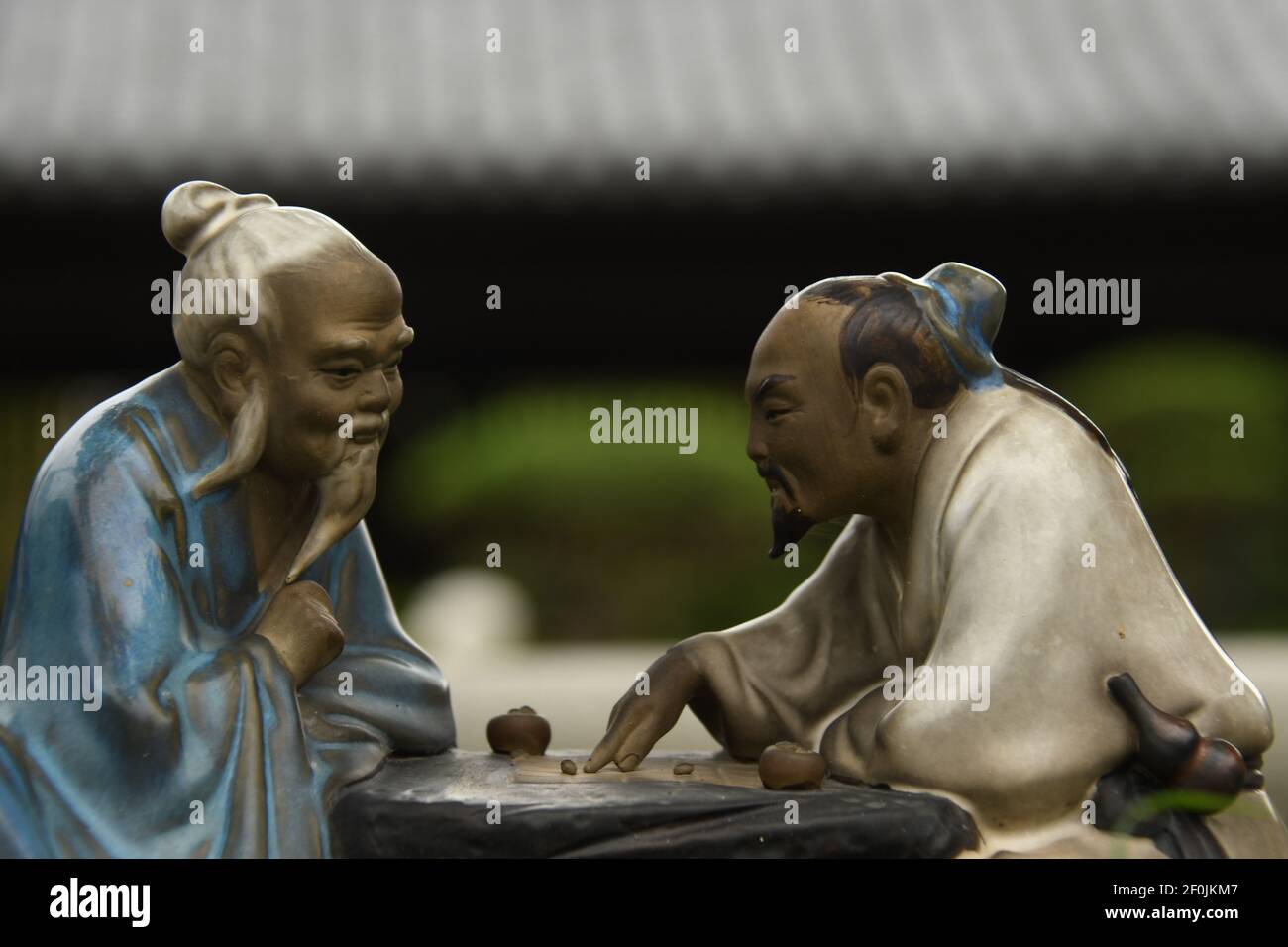 Primo piano di due piccole statue di uomini cinesi che giocano scacchi vicino a un bonsai all'interno del monastero di Chi Lin a Hong Kong Foto Stock