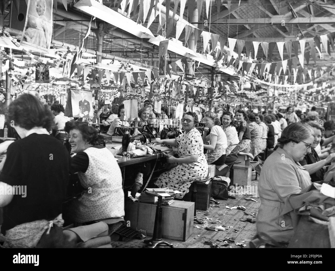 1953, storico, wiorker femminile presso la società di drappeggi, Hepworths di Leeds, Inghilterra, Regno Unito, seduto al lavoro panchine con macchine per la semina. Il pavimento della fabbrica è decorato con conigli e bandiere che celebrano l'incoronazione della Regina Elisabetta II al trono britannico che ha avuto luogo il 2 giugno 1953 all'Abbazia di Westminster. Le opere di Providence su Clay Pit Lane fu la fabbrica di Joseph Hepworth e Son, una compagnia di abbigliamento iniziata nel 1865 e che nel 1905 aveva 143 negozi. Più tardi nel secolo, Hepworths divenne Next. Foto Stock