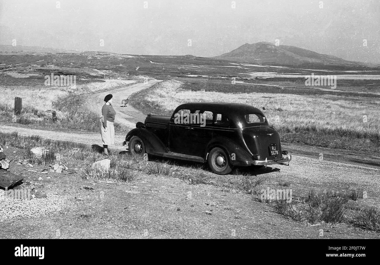 Anni '50, storico, in giro per il Galles in auto, una signora che si trova fuori della sua auto dell'epoca, parcheggiata su una pista di ghiaia sulle pianure ariose e desolanti delle montagne Snowdonia. Foto Stock