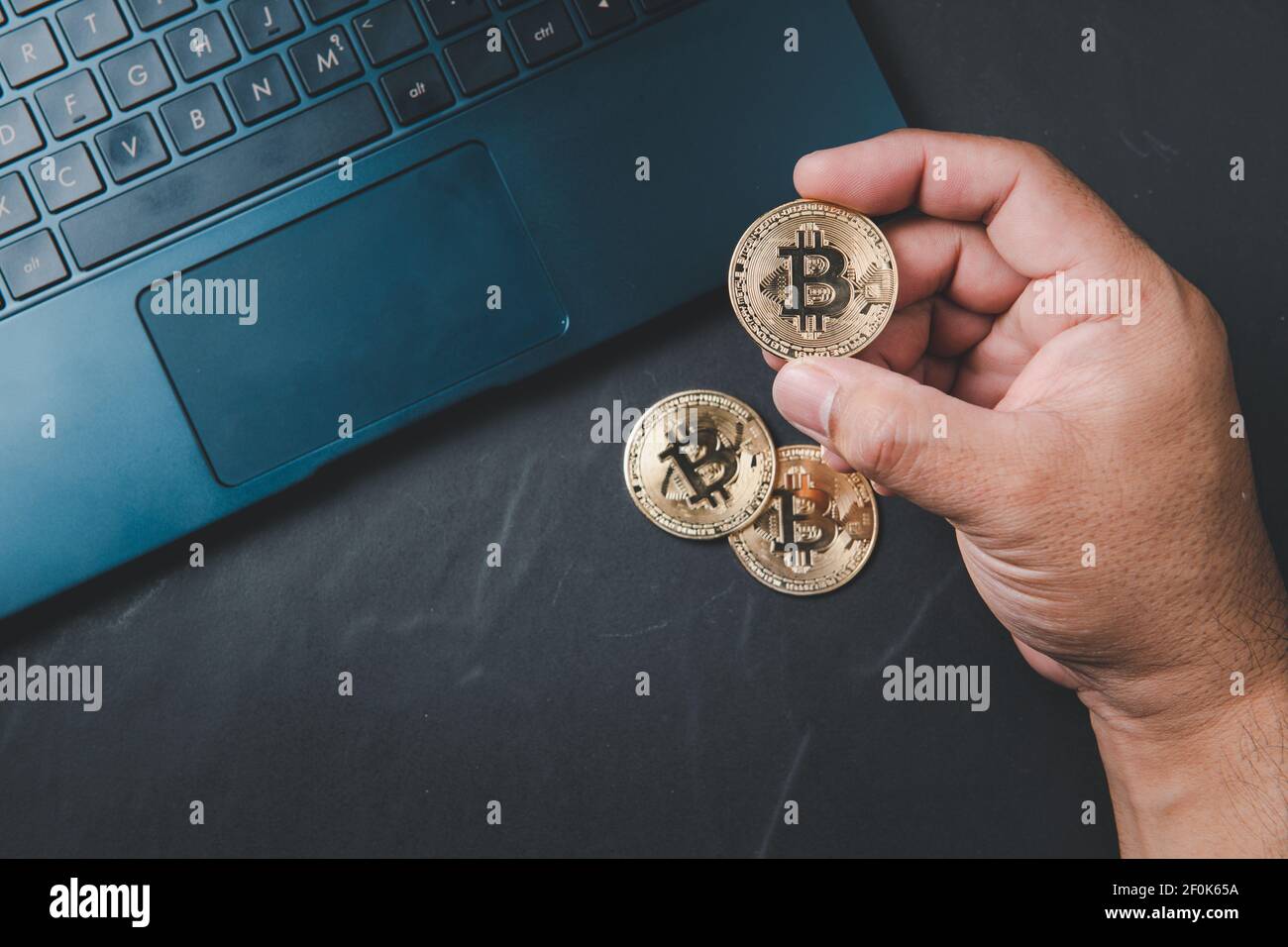 Uomo d'affari che tiene bitcoin e laptop su sfondo nero. Denaro virtuale elettronico per il web banking e il pagamento della rete internazionale, Techn valuta Foto Stock
