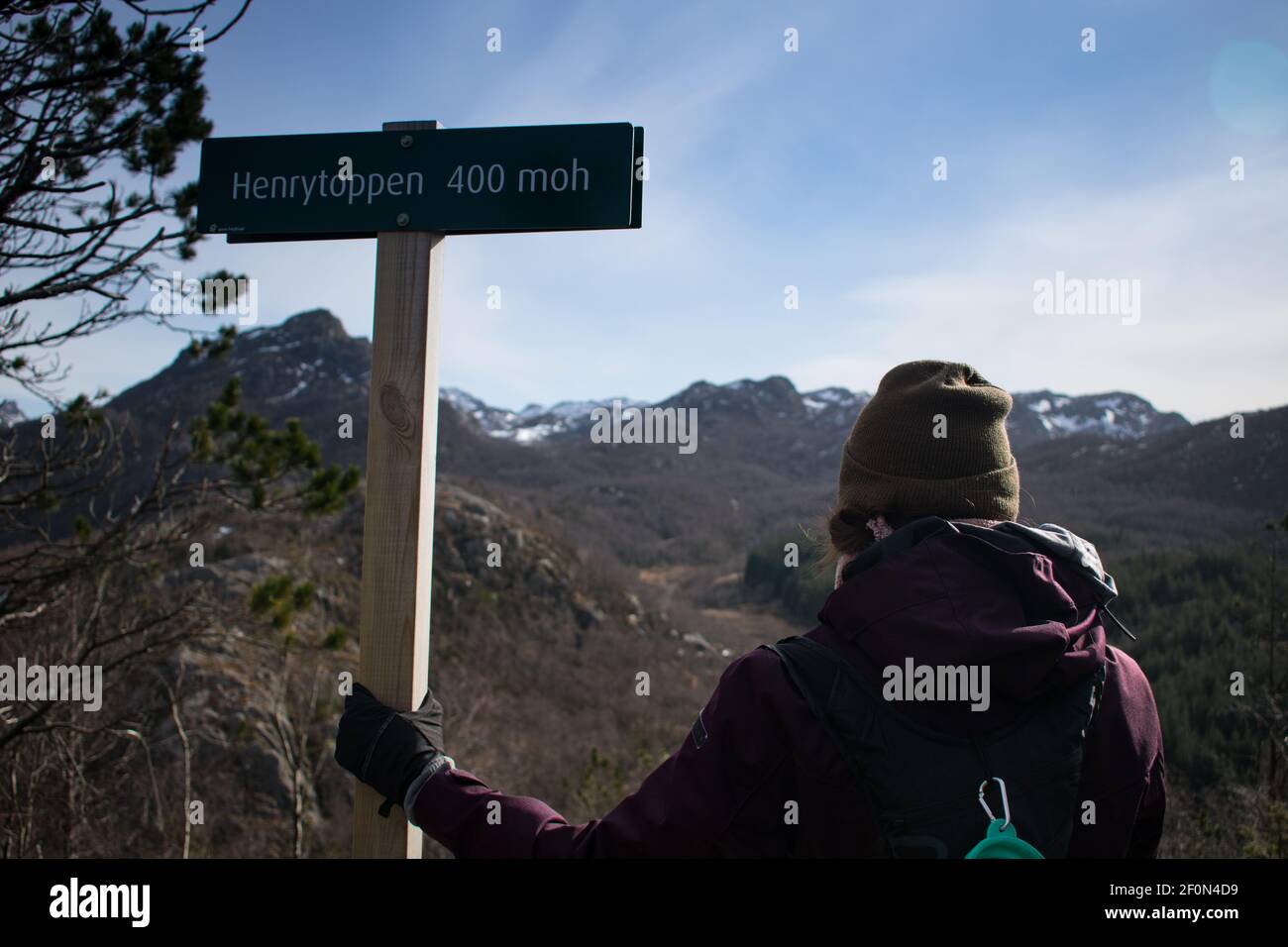 Escursionista femminile che tiene il cartello del sentiero che guarda su una catena montuosa In Norvegia Foto Stock