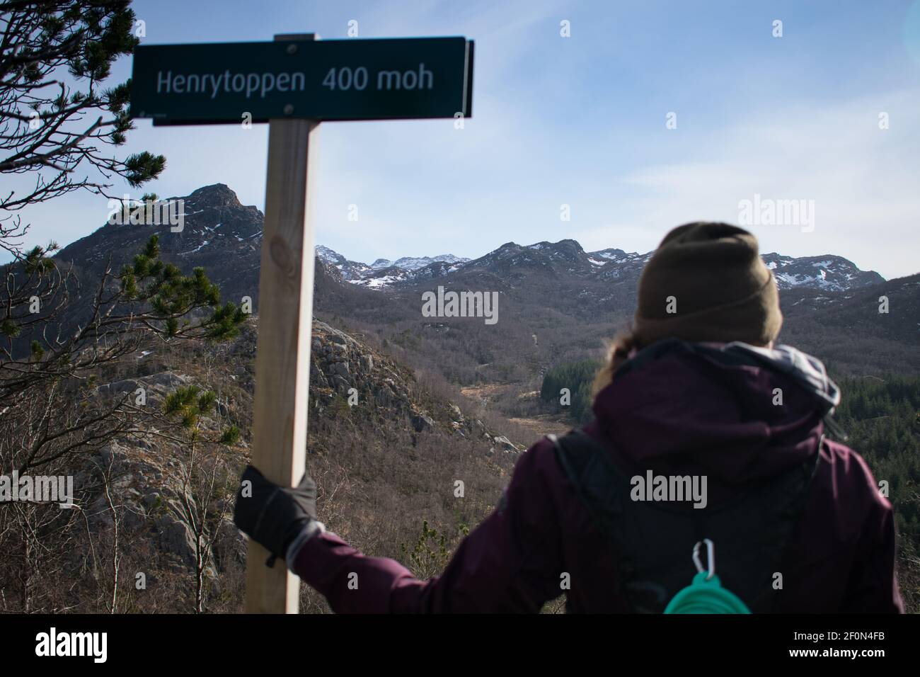 Escursionista femminile che tiene il cartello del sentiero che guarda su una catena montuosa In Norvegia Foto Stock
