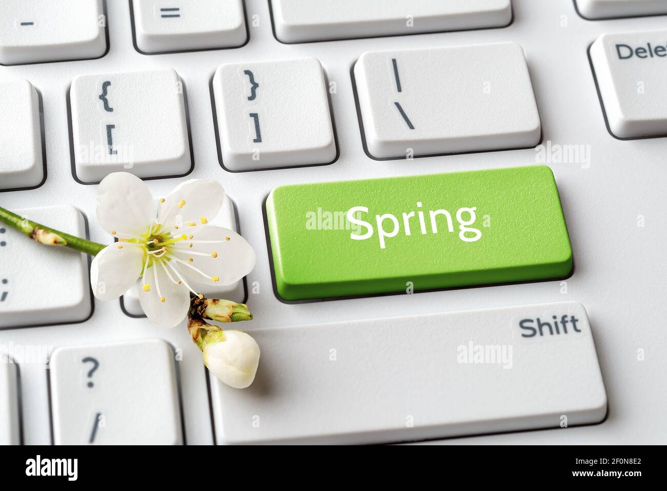 Tasto verde con parola primaverile e fiori di ciliegio sulla tastiera bianca del computer. Umore di primavera, vacanze, concetto di vendita. Messaggio sul pulsante di invio del tastierino. Foto Stock