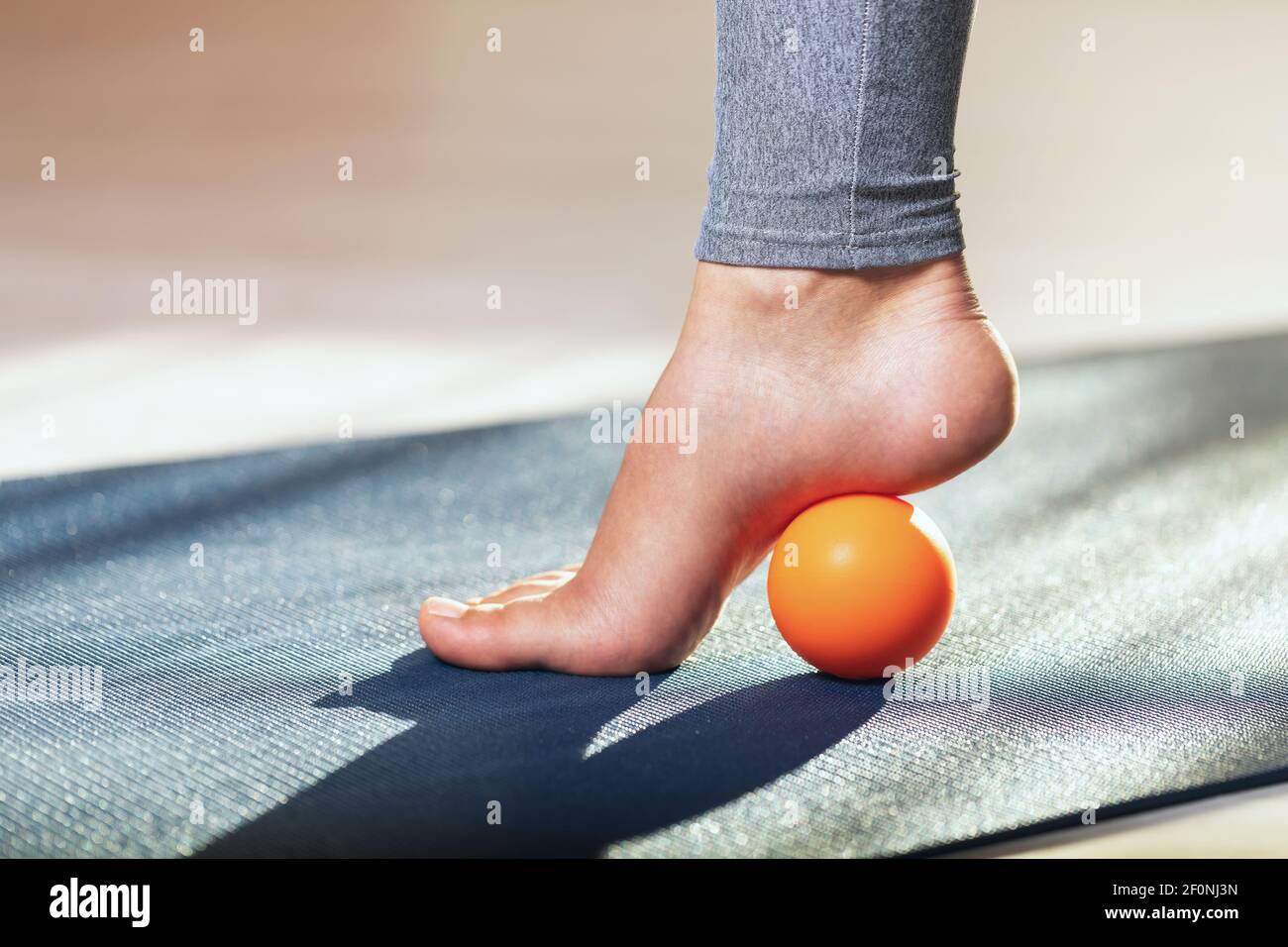 Rilascio miofasciale dei muscoli iper-mobili del piede con una sfera di massaggio su un tappetino ginnico a casa. Prevenzione dell'affaticamento delle gambe dopo un'usura elevata h Foto Stock