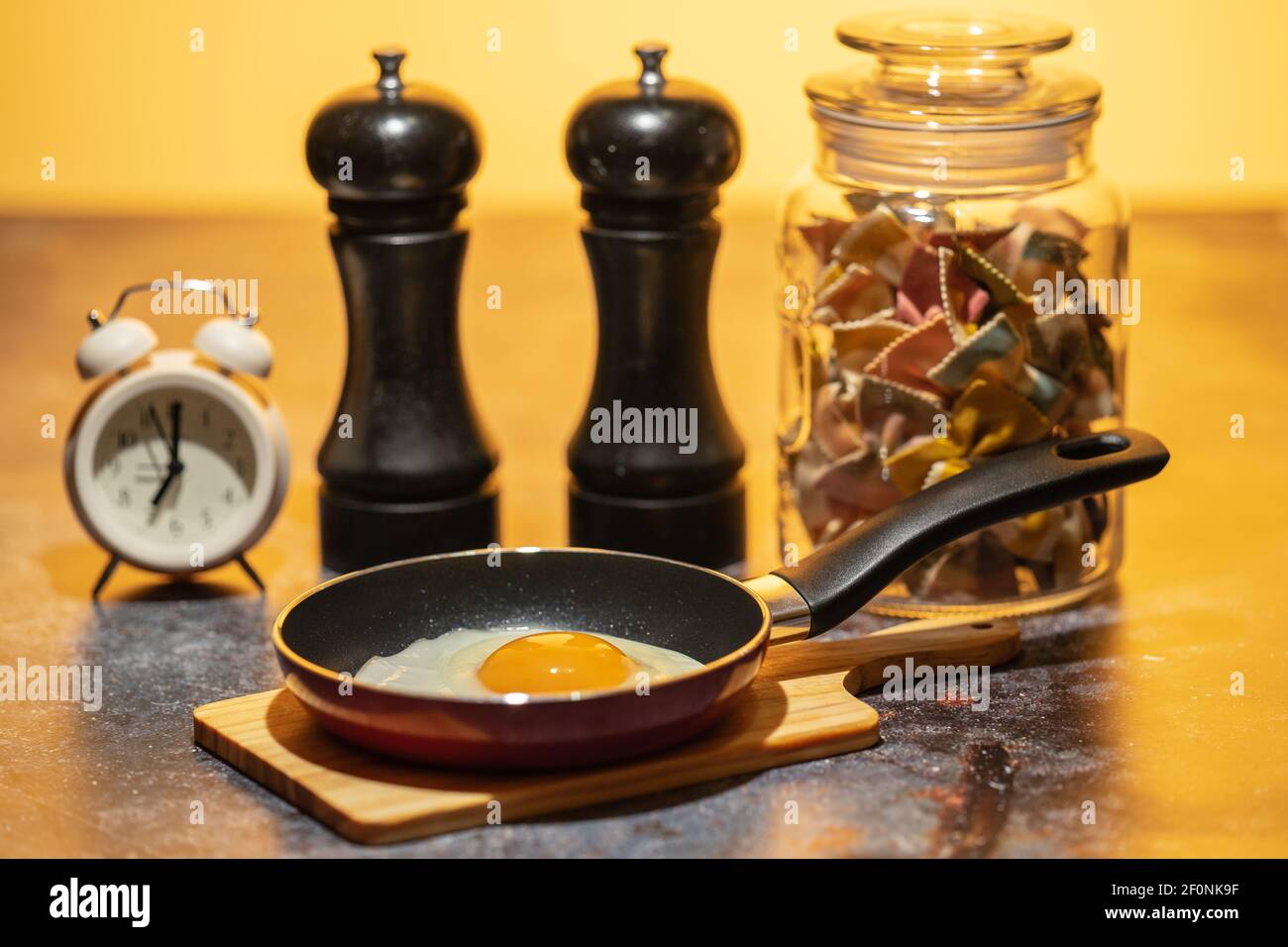 Uova fritte in una padella sul tavolo da cucina accanto alla sveglia. Prima colazione in preparazione Foto Stock