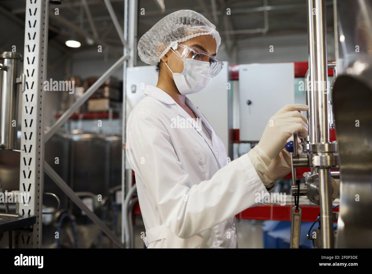 Vista laterale ritratto della giovane operatrice che indossa indumenti protettivi mentre si utilizzano attrezzature presso l'impianto chimico, spazio copia Foto Stock