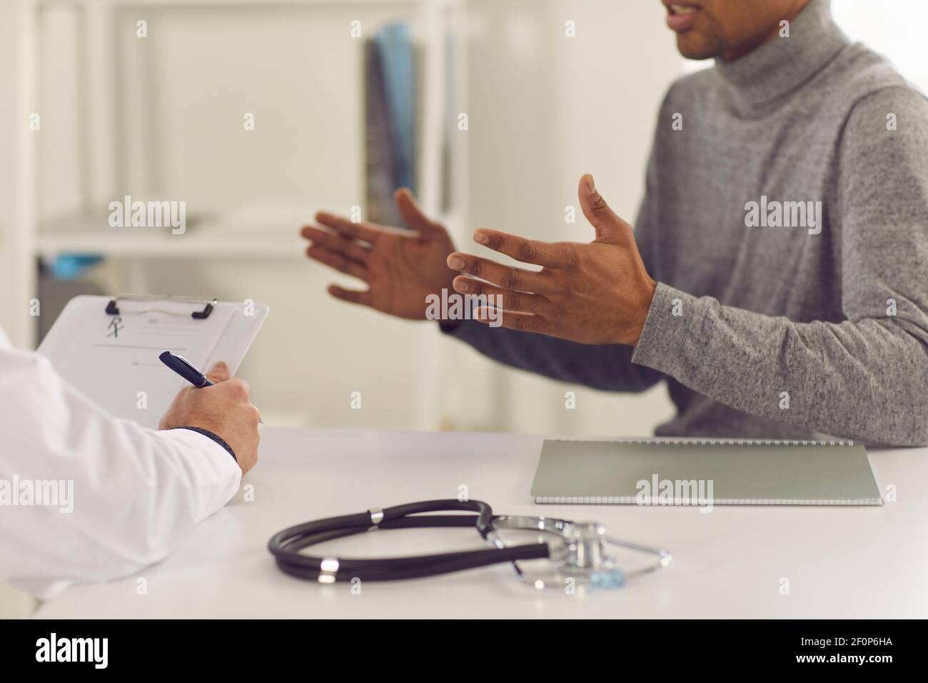 Uomo nero paziente seduta e spiegare i reclami di salute all'uomo medico Foto Stock