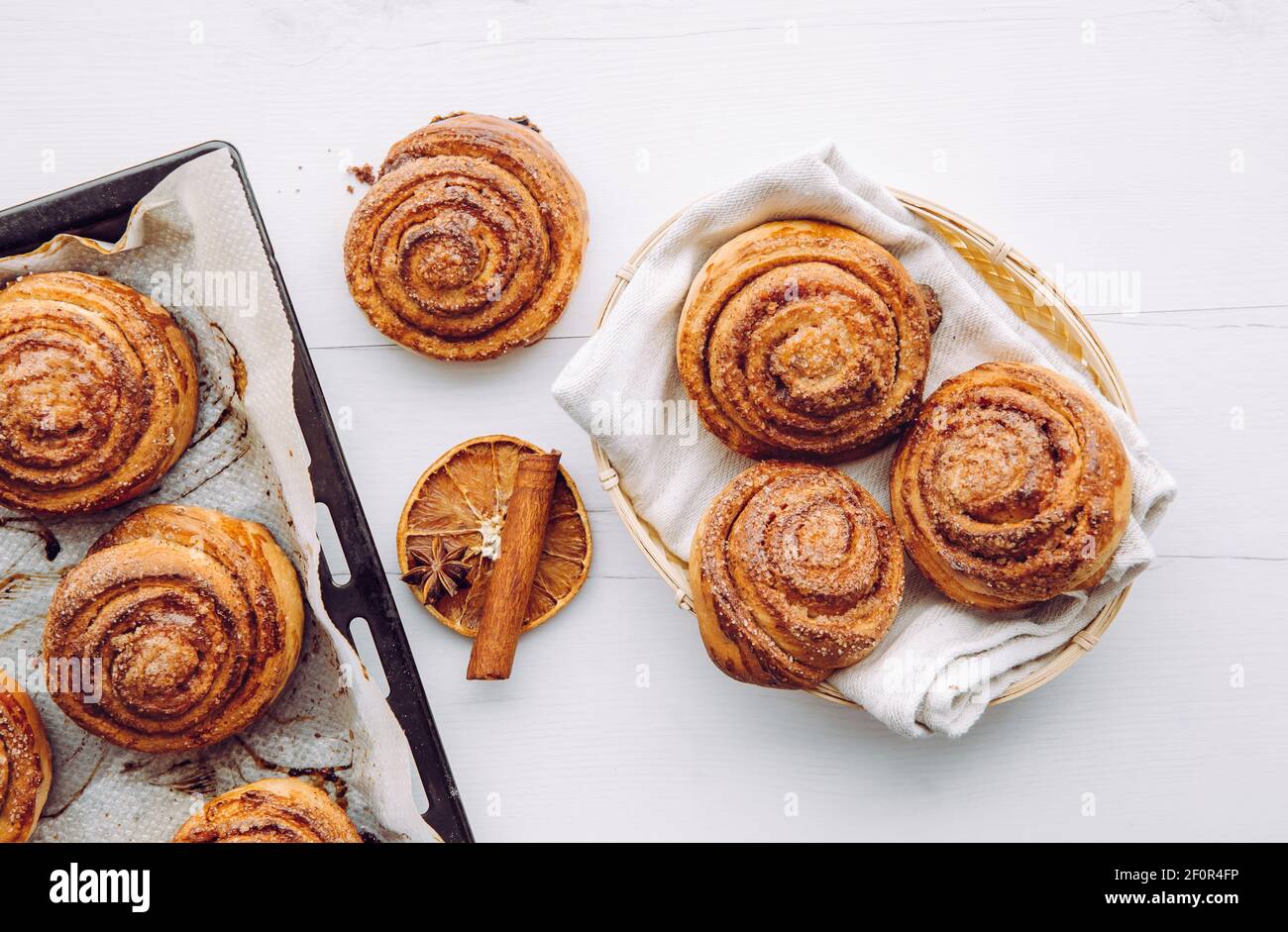 Panini alla cannella fatti in casa appena sfornati in cestino e su una teglia da forno al mattino all'interno, concetto di colazione. Vista dall'alto. Foto Stock