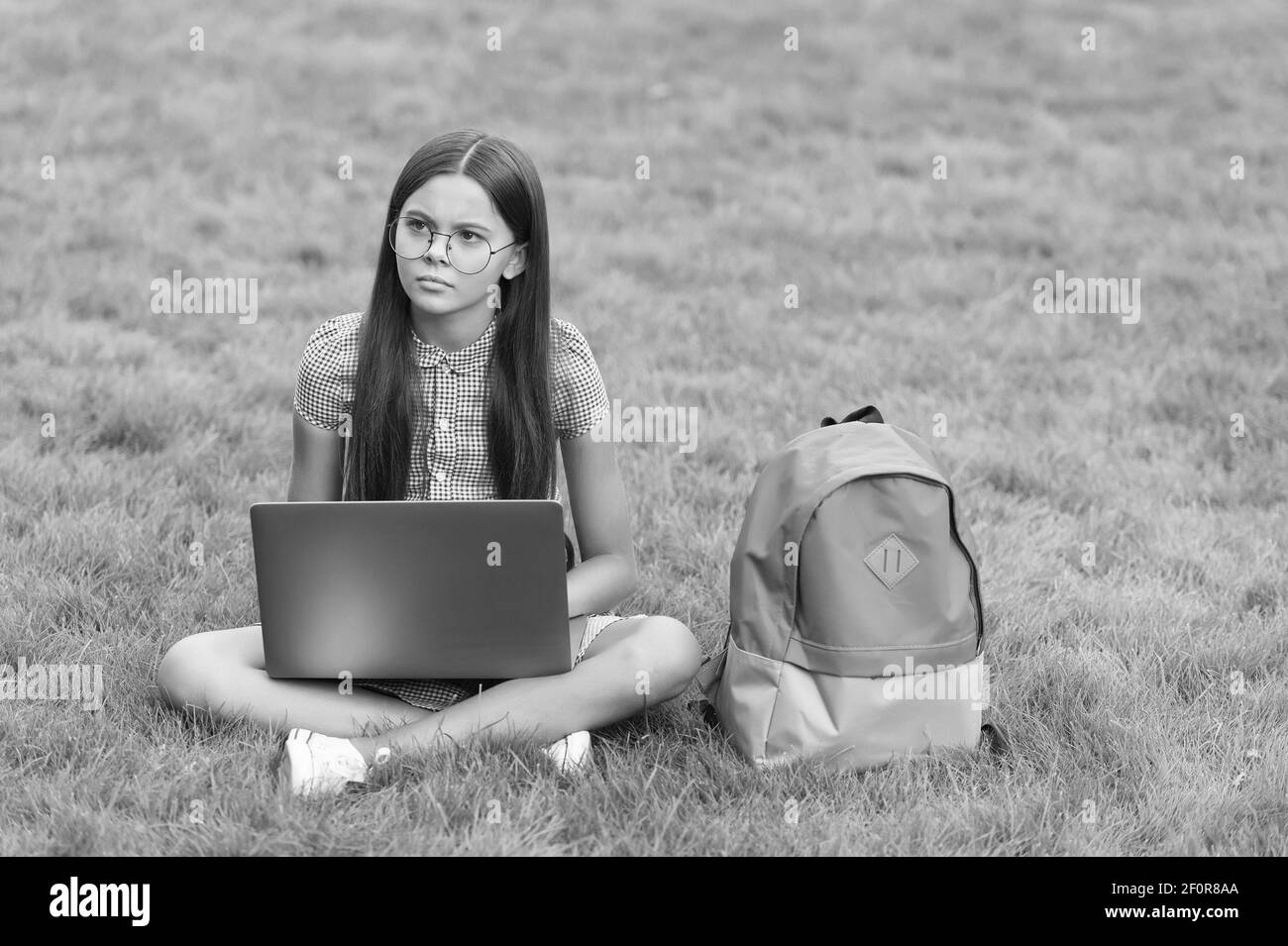 concentrato sull'apprendimento. bambino con zaino e notebook. nuova tecnologia nella vita moderna. lavoro serio per i bambini su laptop. formazione online. ritorno a scuola. ragazza teenager usa il computer su erba verde nel parco. Foto Stock