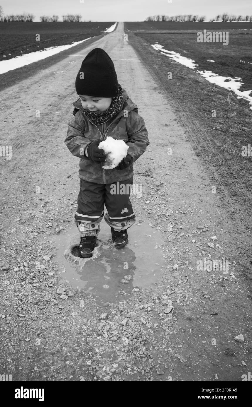 Bambino, ragazzo, 18 mesi, multietnico, passi in puddle, Gioca con palle di neve, risate, Blaubeuren, Baden-Wuerttemberg, Germania Foto Stock