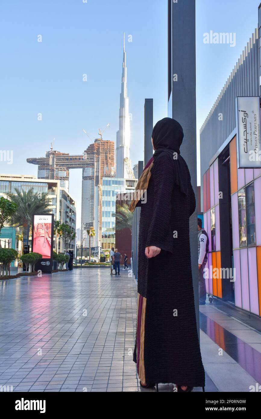 Giovane donna araba che indossa abaya in piedi nella passeggiata della città Dubai e sullo sfondo Burj Khalifa Foto Stock