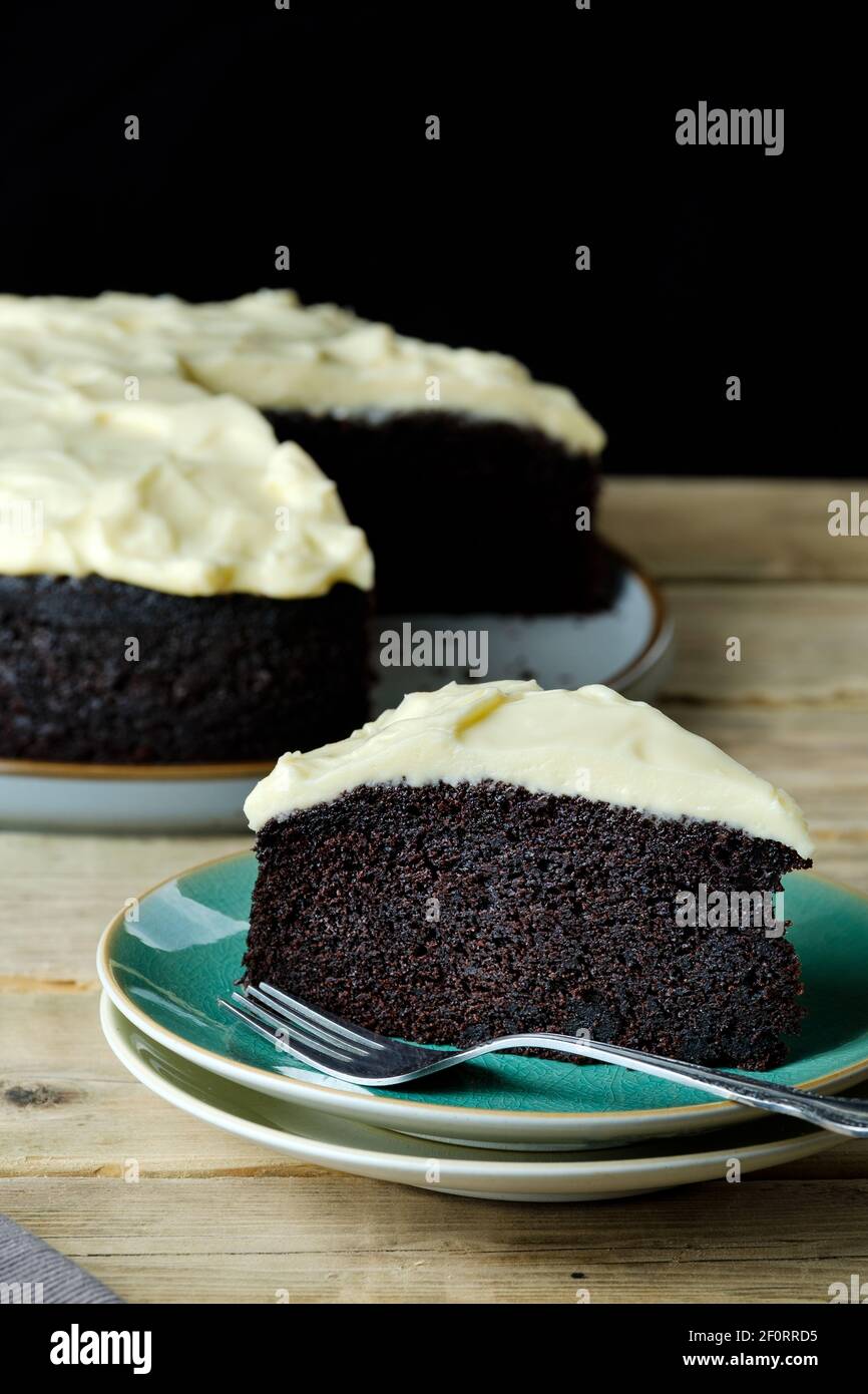 Una fetta, o servire, di Guinness e torta al cioccolato servita su un piatto laterale. La torta principale è mostrata sullo sfondo Foto Stock