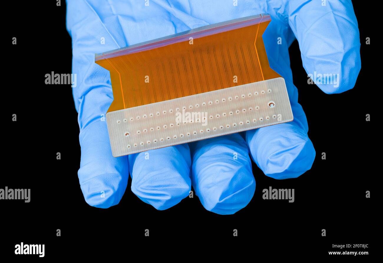 Scheda a circuito stampato flessibile arancione nel dettaglio della mano umana. Ingegnere elettrotecnico con PCB flessibile in plastica per la trasmissione parallela di segnali di dati al pannello LCD. Foto Stock