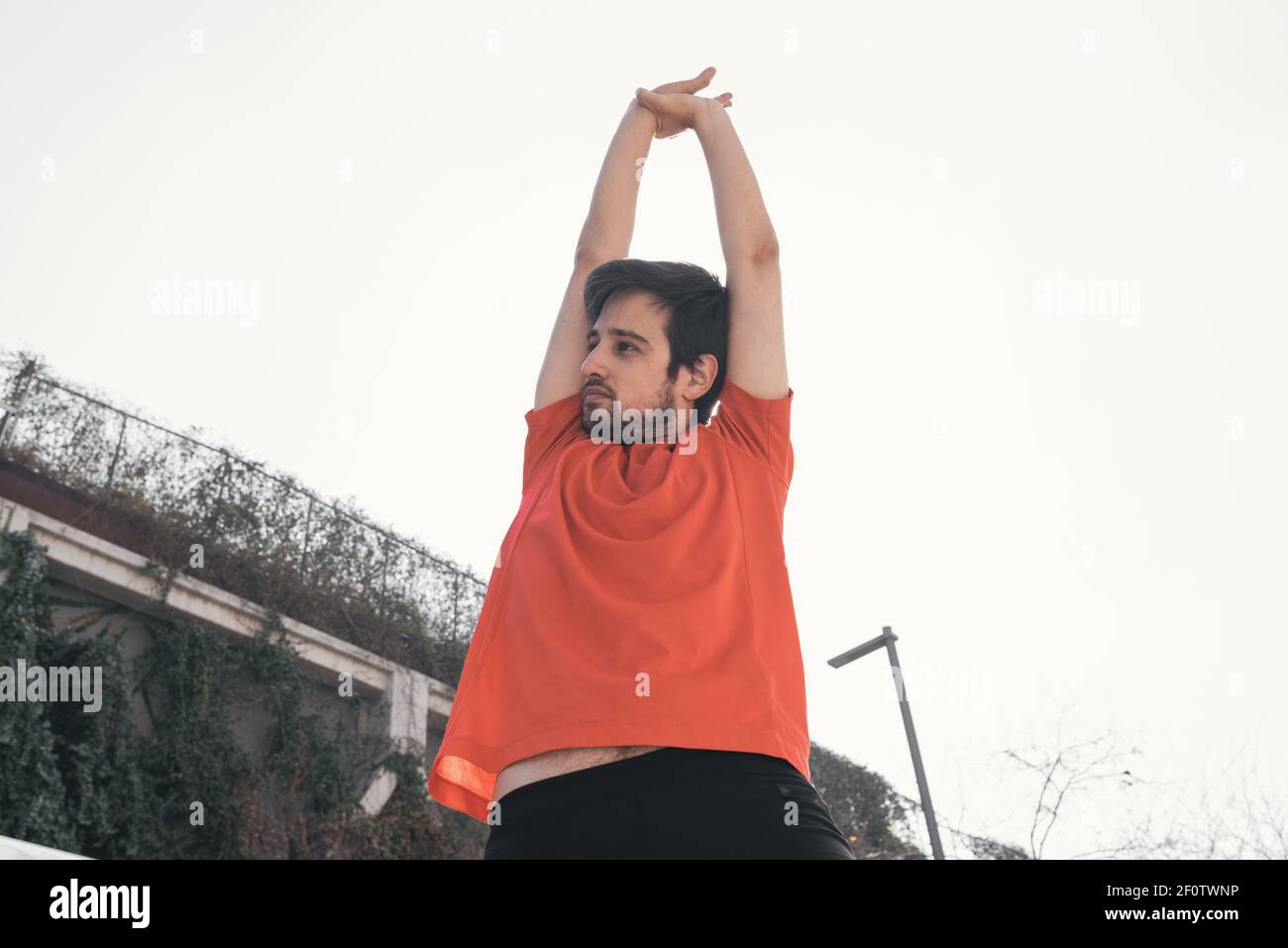 Giovane uomo sportivo che allunga entrambe le braccia sopra la testa Foto Stock