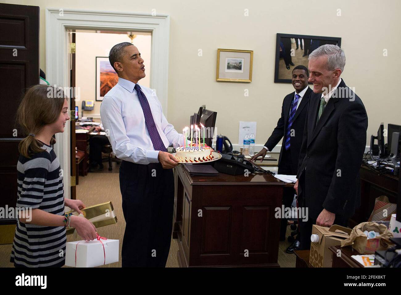 Il presidente Barack Obama, accompagnato dalla figlia del capo dello staff Denis McDonough, porta una torta di compleanno per sorprendere McDonough nell'ufficio del capo dello staff dell'ala ovest, 2 dicembre 2013 Foto Stock