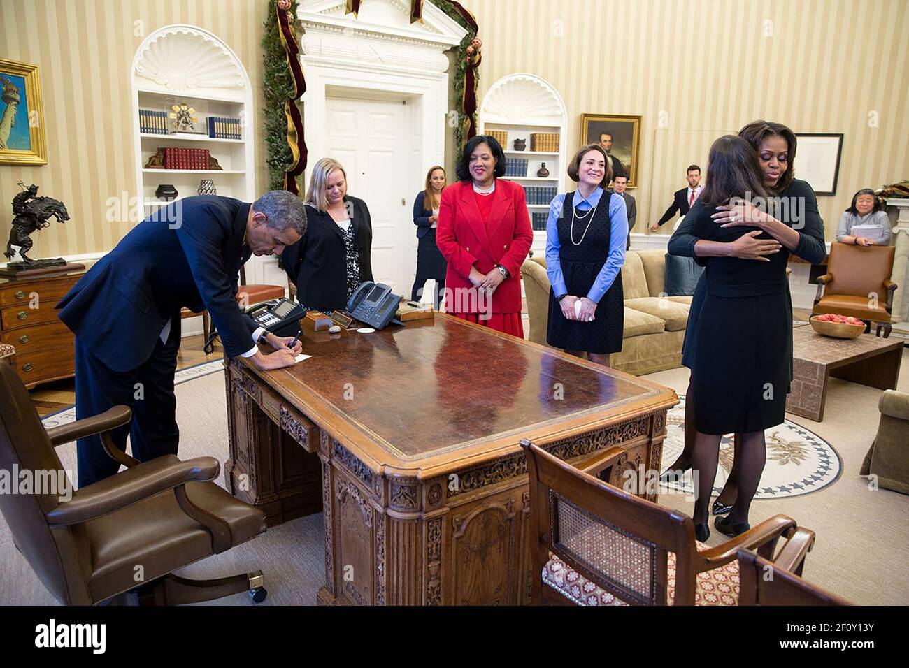 Il presidente Barack Obama firma gli articoli al Resolute Desk dopo che lui e la prima signora Michelle Obama ha incontrato le madri per quanto riguarda l'Affordable Care Act, nell'ufficio ovale, 18 dicembre 2013 Foto Stock