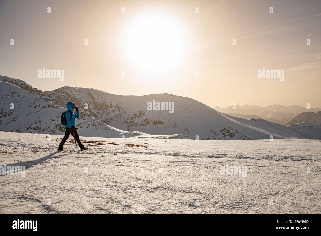 Solo escursionista femminile su un sentiero innevato in cima ad una montagna in inverno con i colori del tramonto nei cieli. Foto Stock